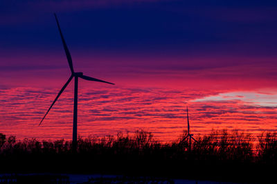Silhouette of wind turbines with red sky during sunset.