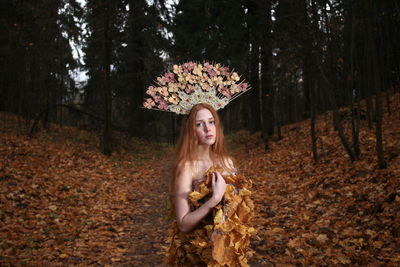 Portrait of young woman wearing flowers on hair standing at forest during autumn
