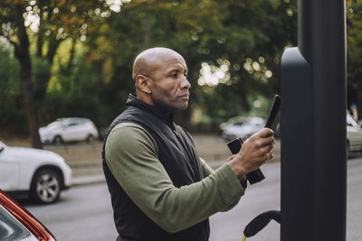 Bald mature man scanning smart phone at charging station