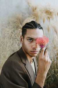 Businessman holding leucospermum flower over face in garden