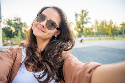 Portrait of smiling young woman wearing sunglasses while standing against trees