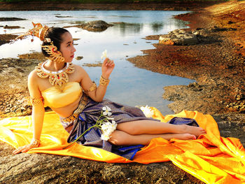 Full length of woman holding flower while sitting at beach