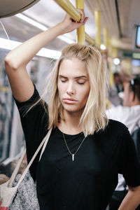 Close-up of tired young woman napping while standing in train