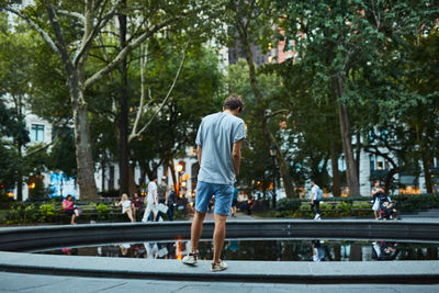 Rear view of young man standing by pond in city