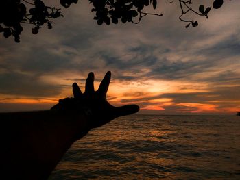 Cropped image of silhouette hand gesturing against sea during sunset