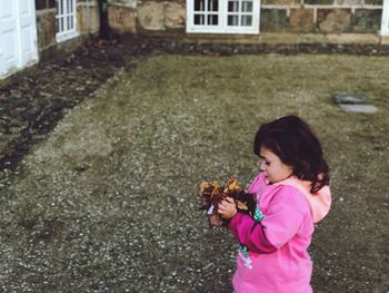 Side view of cute girl holding dry leaves while standing in lawn