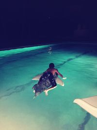 Rear view of shirtless boy surfboarding on swimming pool at night