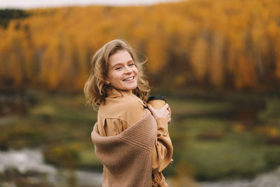 A pretty girl enjoys solitude drinks coffee walks in the autumn forest in nature in fall