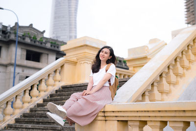 Smiling beautiful woman looking away while sitting on railing