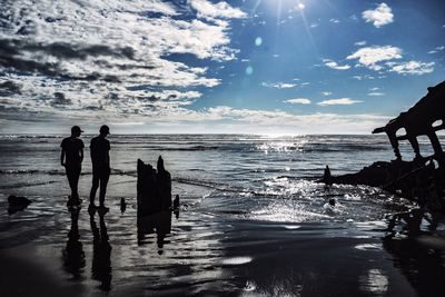 Silhouette people standing on beach against sky