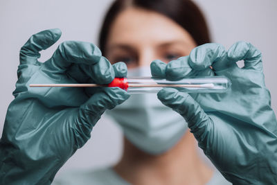 Close-up of doctor wearing mask holding test tube against gray background