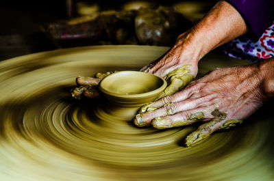 Cropped hands of porter making pot on pottery wheel