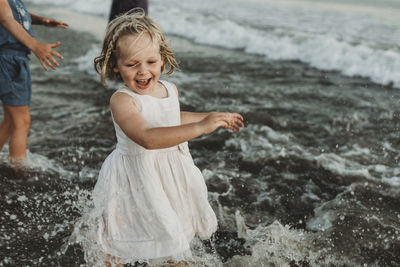 Preschool aged girl in white dress playing in ocean at sunset