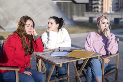Young displeased women sitting by table outdoors