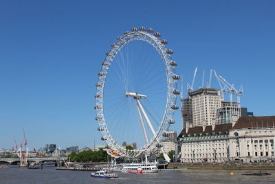 Ferris wheel in city by river against clear sky