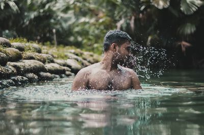 Shirtless man swimming in lake