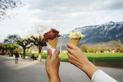 Close-up of hand holding ice cream cone against sky