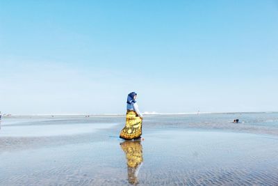 Woman walking at beach against clear blue sky