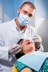 Portrait of male dentist operating female patient in clinic