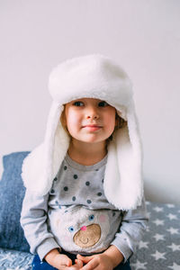 Cute child y on the bed in cozy adult clothes and a hat with earflaps.