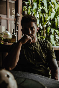 Portrait of young man sitting by plant indoors