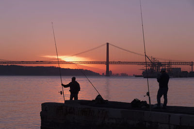 Silhouette bridge over sea against sky during sunset