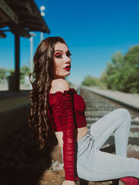 Portrait of young woman sitting on train tracks at station