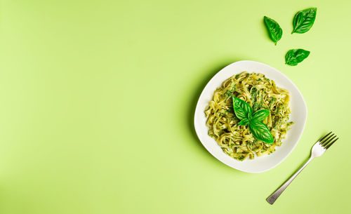 Tagliatelle pasta with pesto sauce, basil and pine nuts on light green background