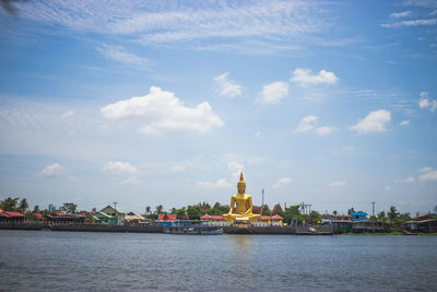 View of buildings by river against cloudy sky