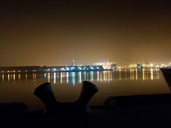 Illuminated city by sea against clear sky at night