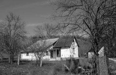 Abandoned house on field by trees against sky