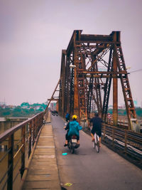 Rear view of man riding bicycle on bridge against sky