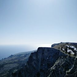 Scenic view of sea by mountain against clear blue sky