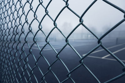 Tennis courts on a foggy park viewed through a fence.