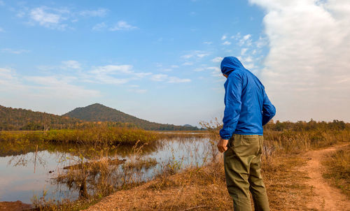 Rear view of man standing by lake against sky