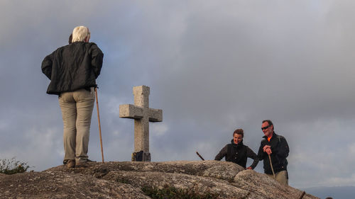 Rear view of men standing on rock against sky