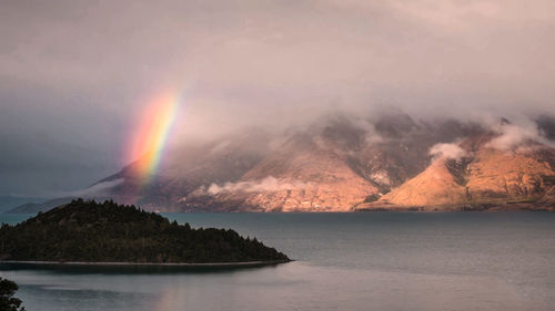 Scenic view of rainbow over sea and mountains against sky