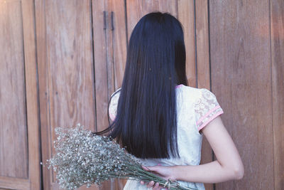 Rear view of woman standing against wooden wall