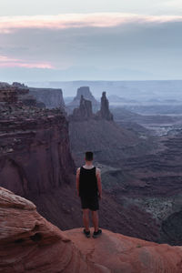 Rear view of man standing on mountain against sky during sunset