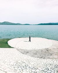 Man standing on shore by sea against sky