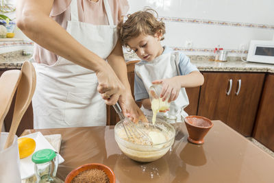 Midsection of mother preparing food with son at home