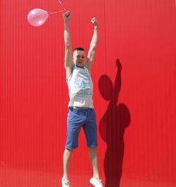 Man with balloons flying against red wall