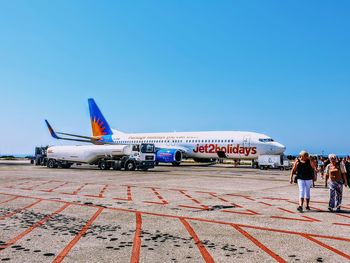 People on airport runway against clear blue sky