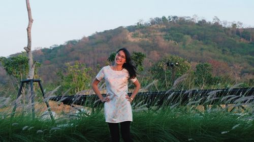 Portrait of young woman standing on grassy field against hill