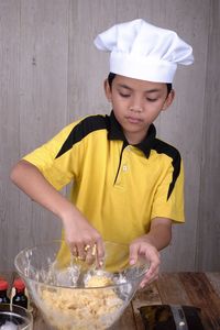 Boy wearing chef hat kneading dough in bowl at home