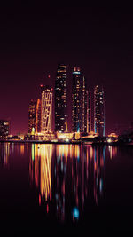 Illuminated buildings by river against sky at night