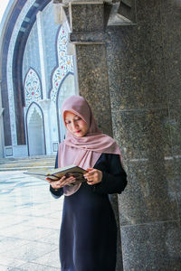 Young woman using mobile phone while standing on wall