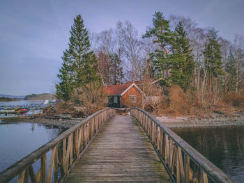 Footbridge over canal amidst trees and buildings against sky