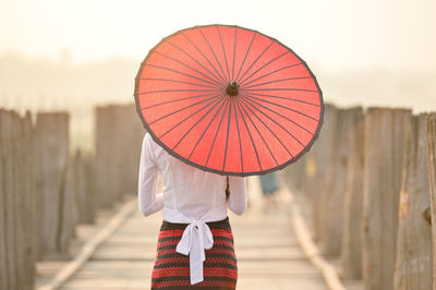 Burmese woman in  traditional costume holding red paper umbrella,