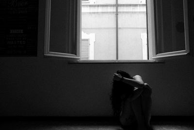 Naked woman sitting on floor against window